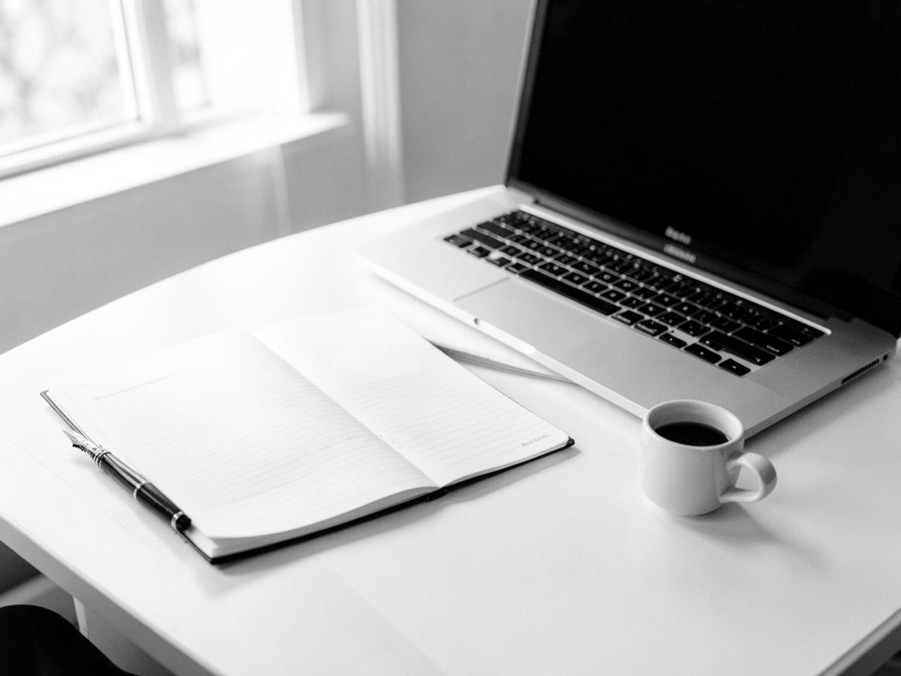 Writing workspace — notebook, pen, laptop, and coffee